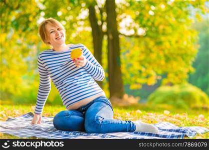 young happy pregnant woman with pear in the park