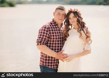 Young happy romantic pregnant couple hugging on nature near lake in summer park. Pregnant woman expecting a baby. Future mom and dad, family. mother&rsquo;s, father&rsquo;s day.. Young happy romantic pregnant couple hugging on nature near lake in summer park. Pregnant woman expecting a baby. Future mom and dad, family. mother&rsquo;s, father&rsquo;s day