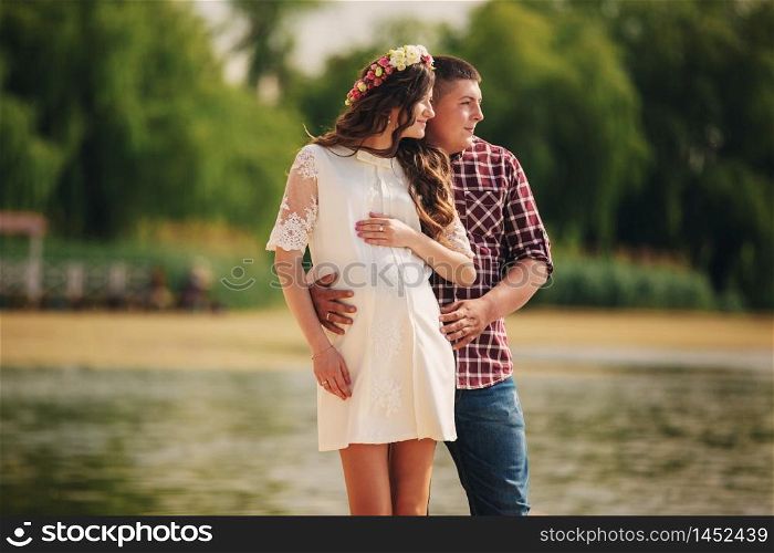 Young happy romantic pregnant couple hugging on nature near lake in summer park. Pregnant woman expecting a baby. Future mom and dad, family. mother&rsquo;s, father&rsquo;s day.. Young happy romantic pregnant couple hugging on nature near lake in summer park. Pregnant woman expecting a baby. Future mom and dad, family. mother&rsquo;s, father&rsquo;s day