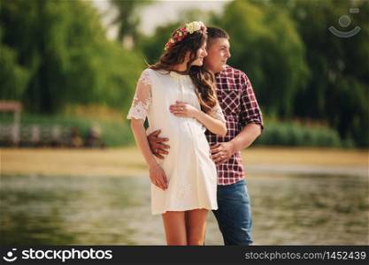 Young happy romantic pregnant couple hugging on nature near lake in summer park. Pregnant woman expecting a baby. Future mom and dad, family. mother&rsquo;s, father&rsquo;s day.. Young happy romantic pregnant couple hugging on nature near lake in summer park. Pregnant woman expecting a baby. Future mom and dad, family. mother&rsquo;s, father&rsquo;s day