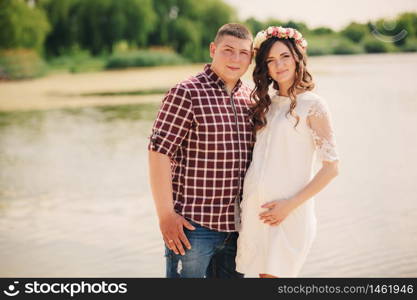 Young happy romantic pregnant couple hugging on nature near lake in summer park. Pregnant woman expecting a baby. Future mom and dad, family. mother&rsquo;s, father&rsquo;s day.. Young happy romantic pregnant couple hugging on nature near lake in summer park. Pregnant woman expecting a baby. Future mom and dad, family. mother&rsquo;s, father&rsquo;s day