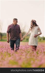 Young happy romantic pregnant couple walking in field of flowers in summer day. Pregnant woman expecting a baby. Future mom and dad, family. mother&rsquo;s, father&rsquo;s day. copy space. Young happy romantic pregnant couple walking in field of flowers in summer day. Pregnant woman expecting a baby. Future mom and dad, family. mother&rsquo;s, father&rsquo;s day. copy space.