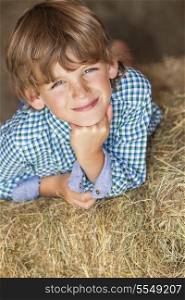 Young happy smiling boy wearing a plaid shirt and laying on bales of hay or straw