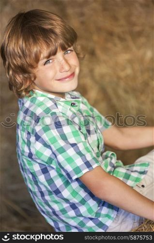 Young happy smiling boy wearing a plaid shirt and sitting on bales of hay or straw