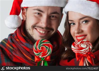 Young happy smiling couple in christmas santa hats with lollipops. Couple in christmas santa hats with lollipops