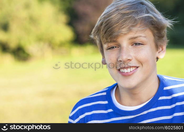 Young happy smiling male boy teenager blond child outside in summer sunshine wearing a blue sweatshirt