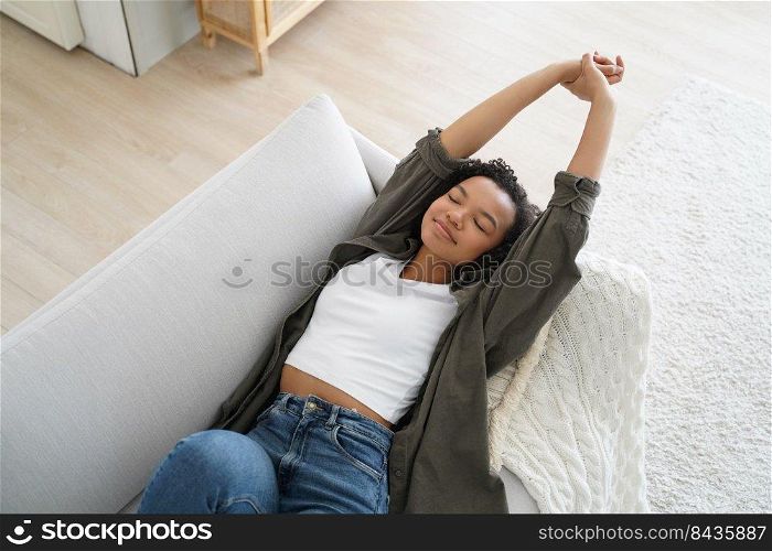 Young happy spanish woman is falling asleep and smiling. Lazy weekend morning of teenager. Attractive afro girl is relaxing on couch at home. Comfort at cosy home in sunday morning.. Young happy woman is falling asleep and smiling. Lazy weekend morning at cosy home.