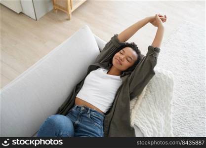 Young happy spanish woman is falling asleep and smiling. Lazy weekend morning of teenager. Attractive afro girl is relaxing on couch at home. Comfort at cosy home in sunday morning.. Young happy woman is falling asleep and smiling. Lazy weekend morning at cosy home.