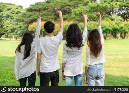 Young happy students of men and women raising hands celebrating and showing teamwork in the park of school or university. Charity, volunteer and unity concept.
