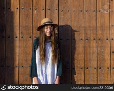 Young happy teenager female with summer clothes standing against old wooden outdoors door while looking at camera