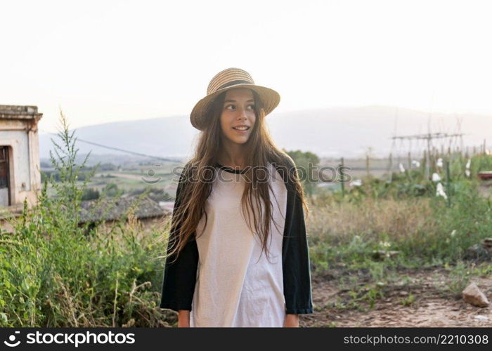 Young happy teenager girl with summer clothes and hat standing in a street outdoors while looking away