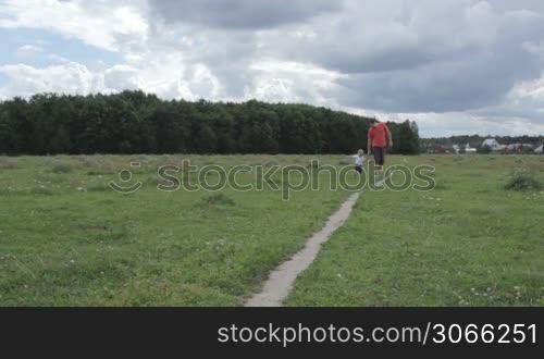 young happy thirty year old father with his son runing across the field and playing.