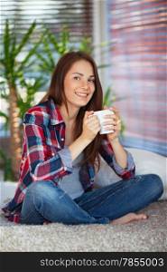 Young happy woman drinking coffee / tea on sofa at home