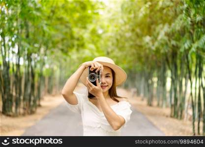 Young happy woman enjoying and taking a photo in the bamboo forest while traveling in summer