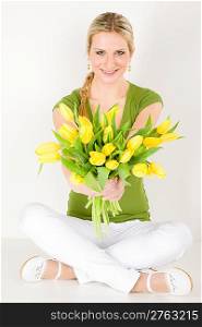 Young happy woman hold bunch of tulips sitting on ground