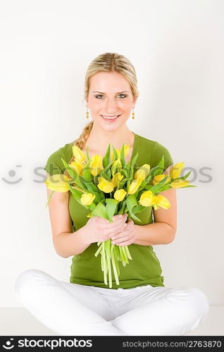 Young happy woman hold bunch of tulips sitting on ground