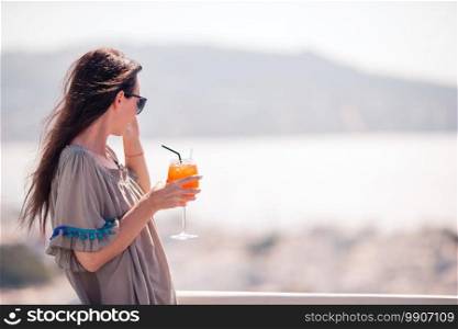 Young happy woman in outdoor cafe with tasty drink. Caucasian tourist enjoy european holidays with amazing view of old city and sea. Young happy woman in outdoor cafe with tasty drink.