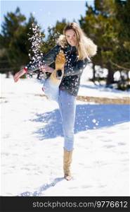 Young happy woman kicking snow in a snow-covered forest in the mountains in Sierra Nevada, Granada, Spain. Female wearing winter clothes playing with snow.. Young happy woman kicking snow in a snow-covered forest in the mountains