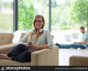 young happy woman sitting on sofa and using mobile phone at luxury home