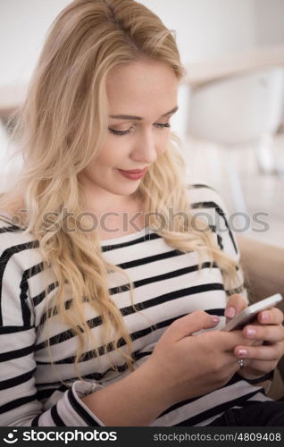 young happy woman sitting on sofa with mobile phone at luxury home