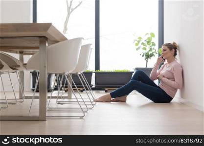 young happy woman sitting on the floor and using mobile phone at home