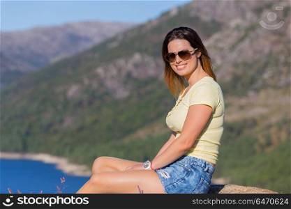 Young happy woman sitting on the rock mountain, relaxing and enjoying the lake at Geres, Portuguese National Park. girl enjoying the lake