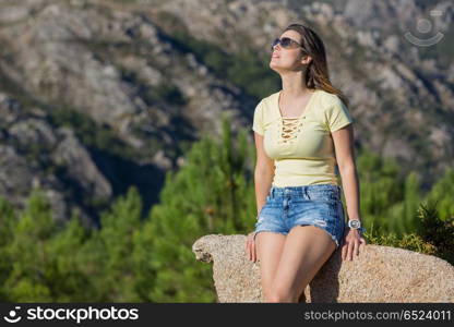 Young happy woman sitting on the rock mountain, relaxing and enjoying the valley view at Geres, Portuguese National Park. girl enjoying