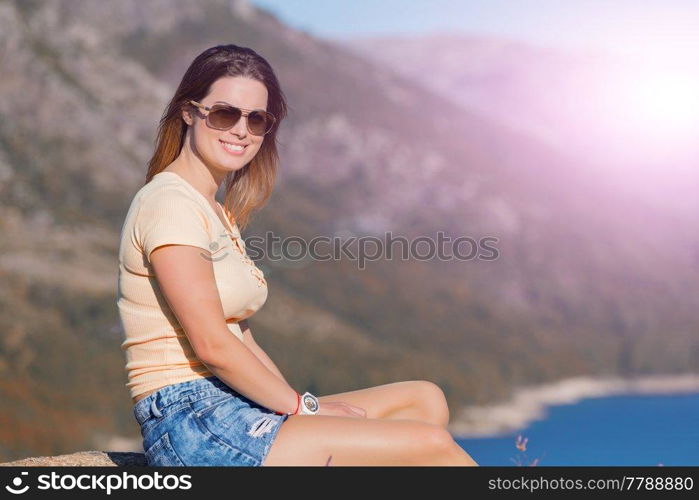 Young happy woman sitting on the rock mountain, relaxing and enjoying the lake at Geres, Portuguese National Park