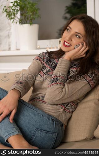 Young happy woman sitting on the sofa at home while talking on phone