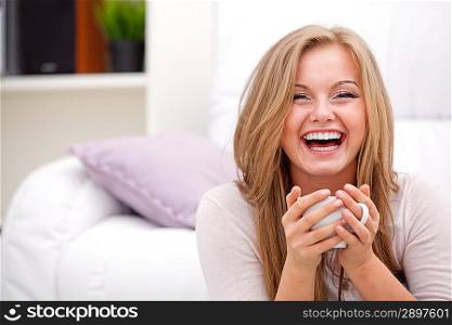 Young, happy woman smiling and holding white cup at home