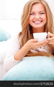 Young, happy woman smiling and holding white cup at home