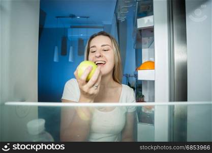 Young happy woman taking green apple out of refrigerator