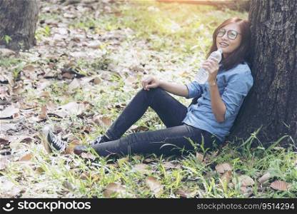 Young happy woman traveler sitting drinking water in the park. Travel Concept.