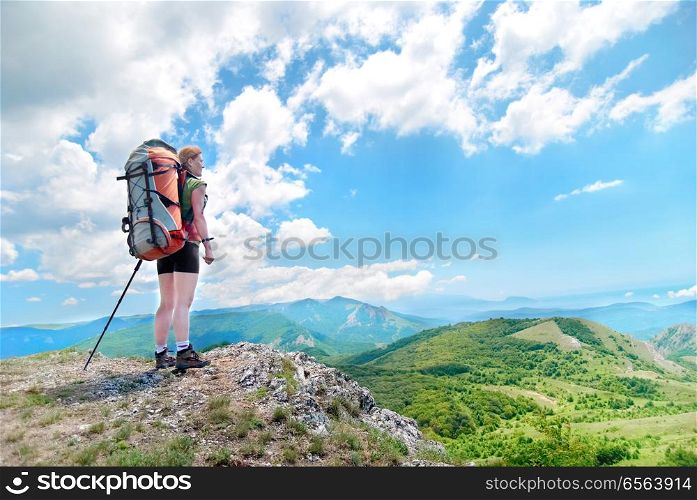 Young happy woman with backpack. Young happy woman with hiking stick and backpack standing on the cliff and looking to green mountains