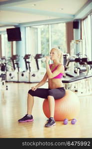 young healthy blonde woman drinking water in fitness gym while sitting on pilates ball. woman in fitness gym drink water