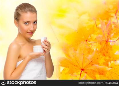 Young healthy girl with body cream jar on autumnal background