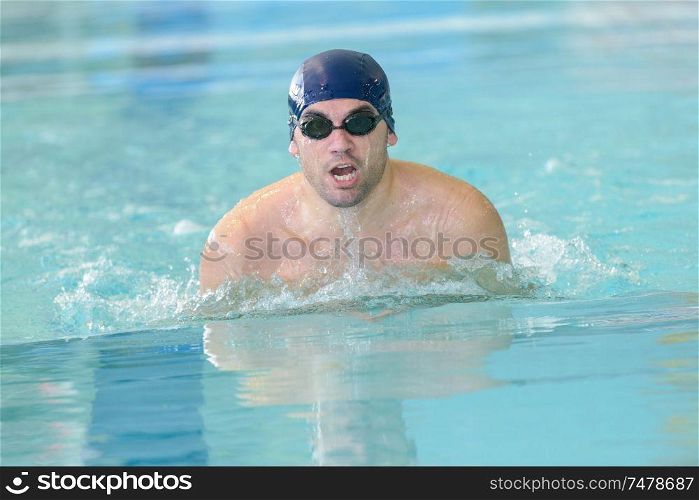 young healthy man with muscular body swims in swimming pool