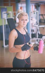 young healthy woman drinking water in fitness gym while sitting on pilates ball and listening music on headphones from smartphone. woman with headphones in fitness gym