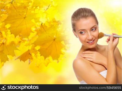 Young healthy woman with makeup brush on autumnal background