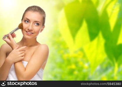 Young healthy woman with makeup brush on spring background