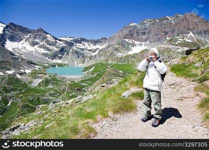 Young hiker taking photographs during a trek in to the Gran Paradiso National Park, Valle d&acute;Aosta, Italy.