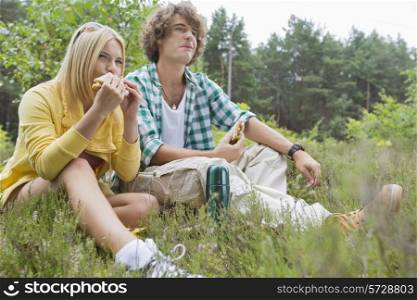 Young hiking couple eating sandwiches while relaxing in field