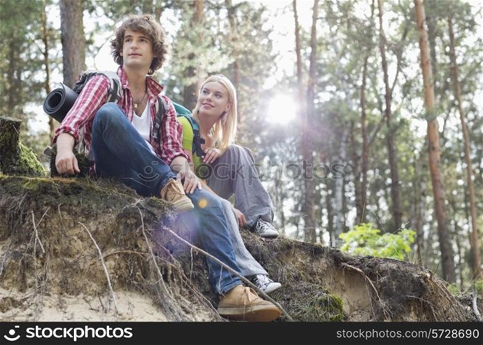 Young hiking couple sitting on edge of cliff in forest