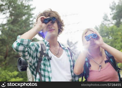 Young hiking couple using binoculars in forest