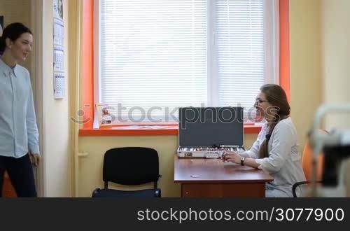 Young hipster couple visiting female ophthalmologist in modern clinic. Beautiful woman in the optometrist office examining her eyesight. Friendly ophthalmologist in uniform welcoming patients in oculist office. Eye care concept.