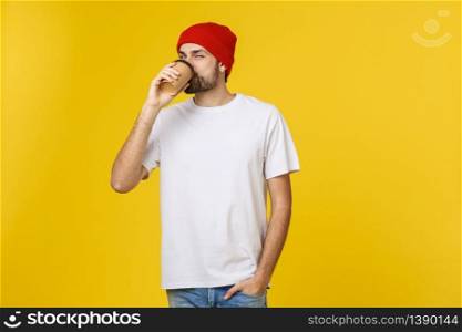 Young hipster man holding a cup of coffee isolated over yellow background. Young hipster man holding a cup of coffee isolated over yellow background.