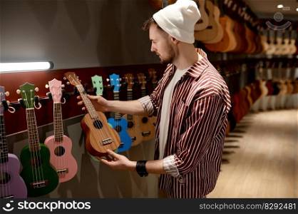 Young hipster man musician buying ukulele guitar at musical instrument shop store. Hobby, business and commerce concept. Man musician buying ukulele guitar at musical instrument shop