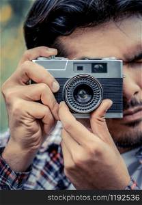 Young hipster man taking photo with old style camera with nature landscape background. Retro and vintage photography concept.
