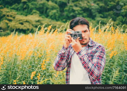 Young hipster man taking photo with old style camera with nature landscape background. Retro and vintage photography concept.