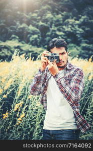 Young hipster man taking photo with old style camera with nature landscape background. Retro and vintage photography concept.